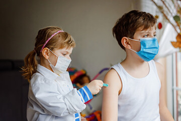 Little girl makes injection to brother, school kid boy. Children, siblings with medical mask...