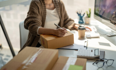 Online sales business woman owner is taking note of the customer's address on the parcel box being...