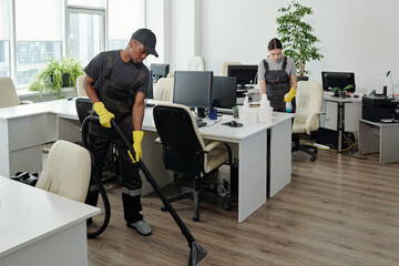 Two young workers of contemporary cleaning service company in coveralls and gloves carrying out...