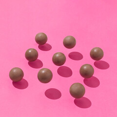 Creative composition made of brown chocolate balls with sunshine shadows on vibrant pink background. Minimal food concept.