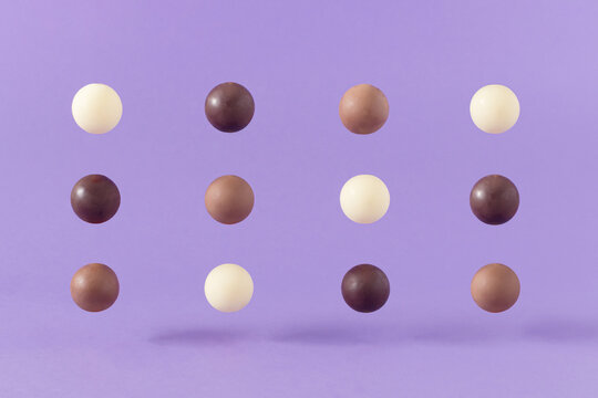 Trendy composition made of neatly arranged levitating brown, black and white chocolate balls against purple background. Minimal candy food concept. Creative dessert idea.