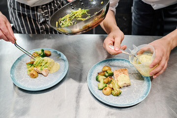 Close-up of chef putting dish on plates with his assistant pouring sauce on dish at table