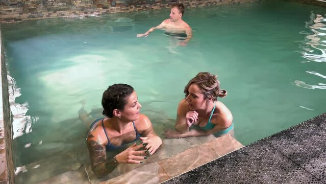 Young adult women chatting in spa pool while strong man shows up