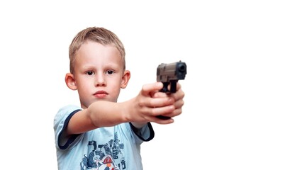 Focused schooler stretches out hands holding toy pistol on white background. Cute blond boy imitates shooting with gun at home close view - 500970846