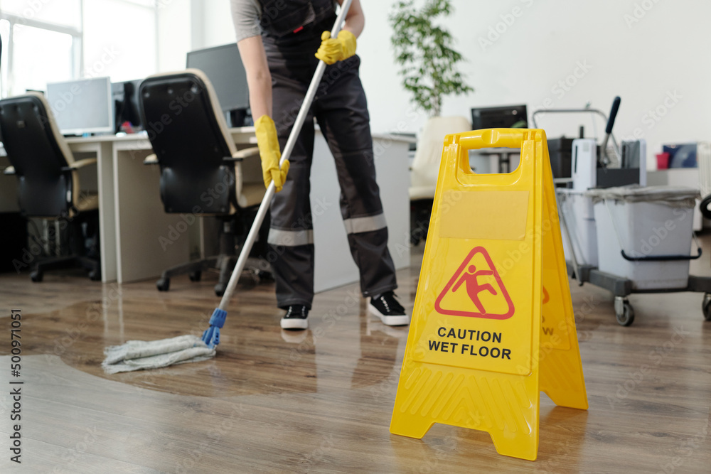 Poster yellow plastic signboard with caution warning about wet floor and female cleaner in black uniform wo