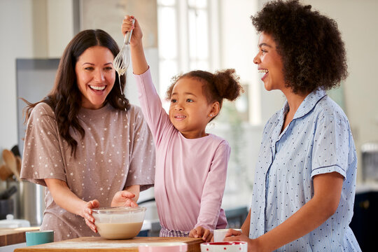 Family With Two Mums Wearing Pyjamas Making Morning Pancakes In Kitchen At Home With Daughter