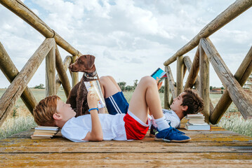 Two children reading books on a bridge with their dog