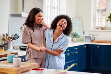 Loving Same Sex Pregnant Female Couple Wearing Pyjamas Dancing In Kitchen At Home