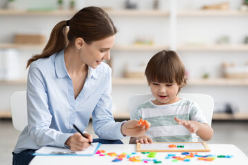 Preschool education concept. Professional woman teacher exercising with little pupil, cute boy reading English letters