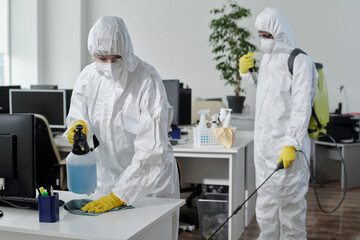 Contemporary disinfection service company staff in protective workwear carrying out their work in...
