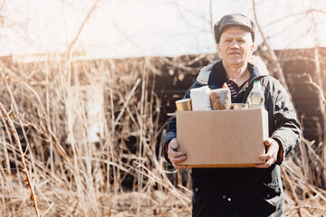 Old man senior is holding cardboard box of donations canned food, looking camera. Concept...