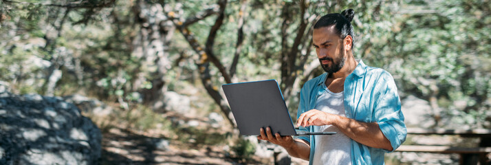 Male tourist working on a laptop outdoors in a camping.