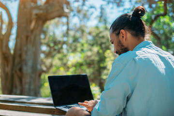 Male tourist working on a laptop outdoors in a camping.