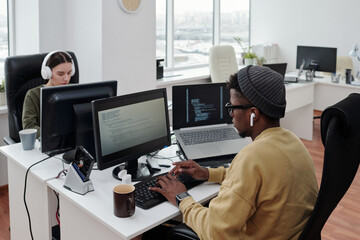 Contemporary intercultural programmers sitting in front of computers in large openspace office and working over new software