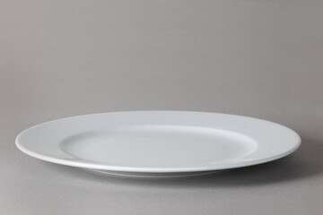 Flat front angle view of a white dinner plate on neutral background with shadow