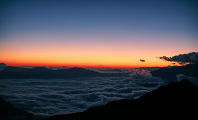 High angle shot of a sea of clouds at dawn viewed from a mountain top after a long trek. A silhouette scene that provokes calmness, positive vibe, mindfulness and suitable for text background.