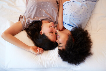 Overhead Portrait Of Loving Same Sex Female Couple Wearing Pyjamas Lying On Bed At Home