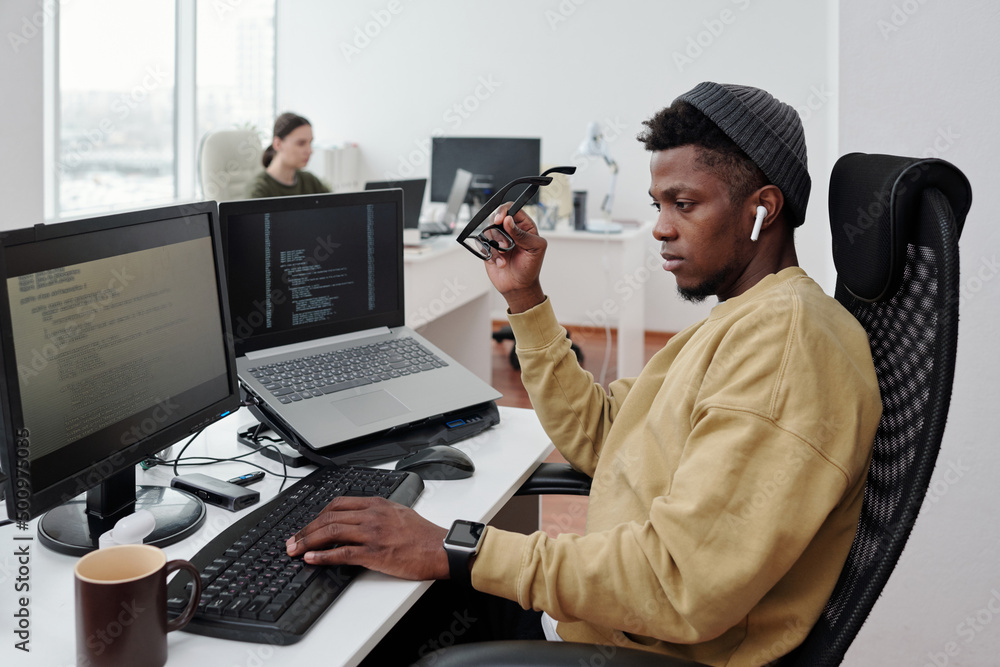 Aufkleber Young contemporary African American it-engineer decoding data by workplace in openspace office while looking at computer screen