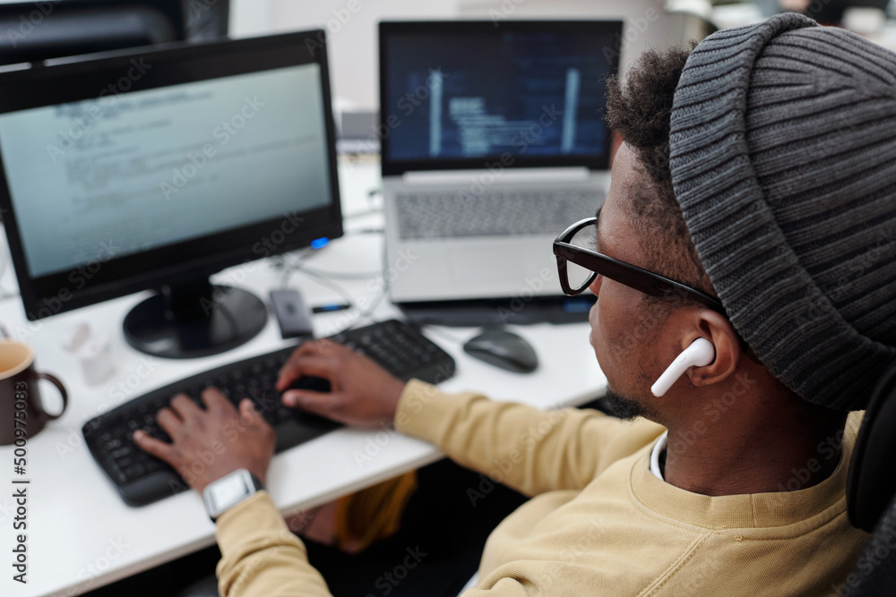 Aufkleber above angle of young black man in casualwear listening to music in earphones while decoding data in 