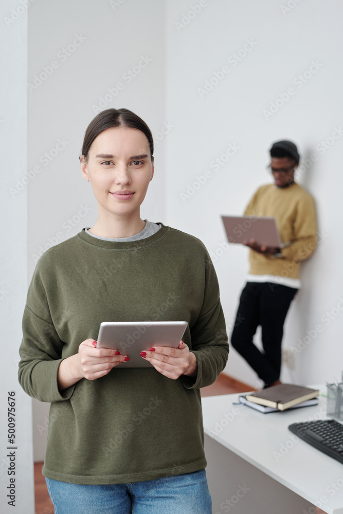 Poster young confident female manager or programmer in casualwear using tablet while working over new proje