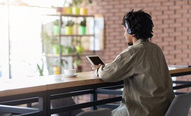 Fototapeta premium Serious young black curly guy in wireless headphones looking at tablet with blank screen