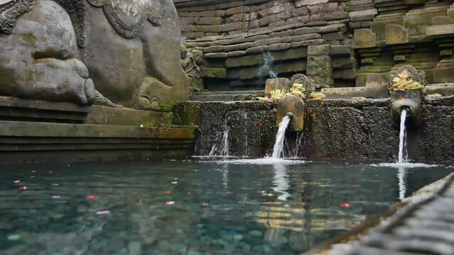 BALI, INDONESIA - JANUARY 24, 2018: Spring streams with gods offerings in Pura Tirta Empul Temple. 4K, Handheld. Low angle