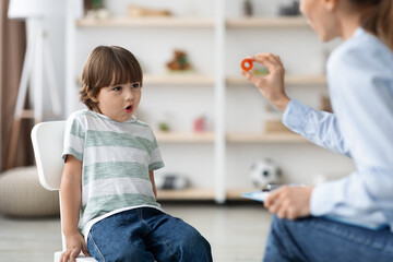 Cute little boy studying with professional woman speech therapist, pronouncing sound O at classroom