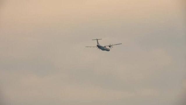 Turboprop unrecognizable plane flies in the sunset sky, long shot bottom view. Air industry, travel and tourism concept