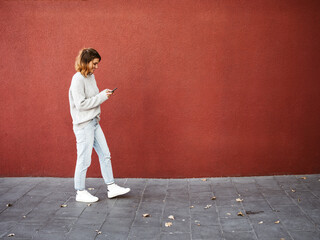 young woman walking with her cell phone in front of red wall