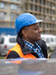 Profile portrait of a smiling Indian engineer or factory worker wearing a safety helmet and looking to the side
