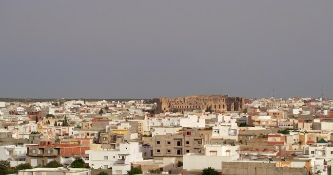Aerial Upward Shot Of El Jem Amphitheater In Residential Town Against Clear Sky - El Djem, Tunisia