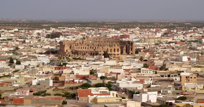 Aerial Shot Of Famous El Jem Amphitheater Amidst Houses In Town, Drone Flying Forward On Sunny Day - El Djem, Tunisia