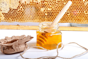 Jar with fresh honey and honeycombs on a white table against the background of a frame with...