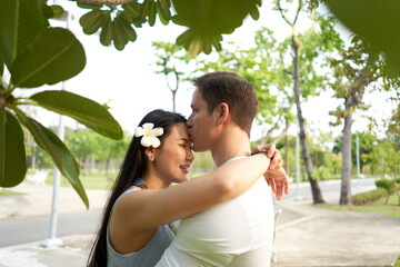 Fototapeta premium Man kissing a woman with a flower in the hair in the middle of a park