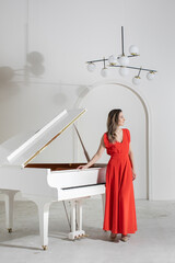 Portrait of young elegant musician woman in red dress by the grand piano on white background