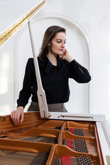 Portrait of a young elegant female musician in a red dress made through a raised piano lid on a white background