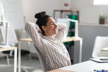 Calm female company employee leaning on chair with hands behind head, relaxing after completed job...