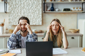 Unhappy young european couple have stress, think and suffer from headache, pay bills and taxes at...