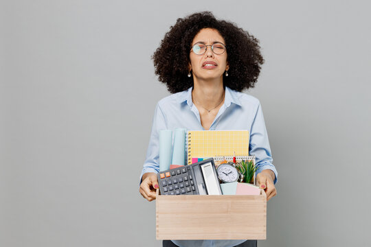 Young stressed unhappy employee business corporate lawyer woman of African American ethnicity in classic formal shirt work in office hold cardboard box with stuff isolated on grey background studio.