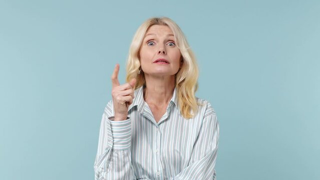 Smart elderly blonde woman lady 40s years old wears white shirt looks around thinks scratches at temple comes up with ideas raised finger isolated on plain pastel light blue background studio portrait