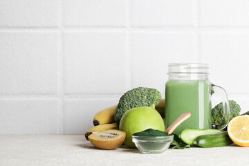Obraz na płótnie Canvas green smoothie in glass bottle, spirulina powder, vegetables and fruits on white ceramic tile background. healthy, raw, vegan diet concept. copy space