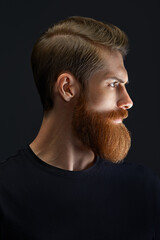 Dramatic light portrait of confident young bearded man looks into the distance. Side view portrait...