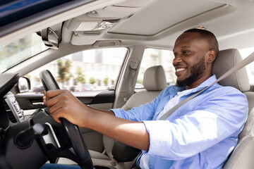Smiling black guy driving new car in city