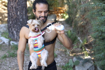 Shirtless man using cute dog carrier using feeding bottle