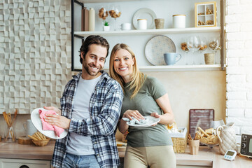 Cheerful young european lady and male washing dishes in modern kitchen interior. Hygiene, household...