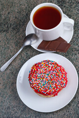 fresh delicious donut with colorful sprinkles and a cup of black tea for breakfast