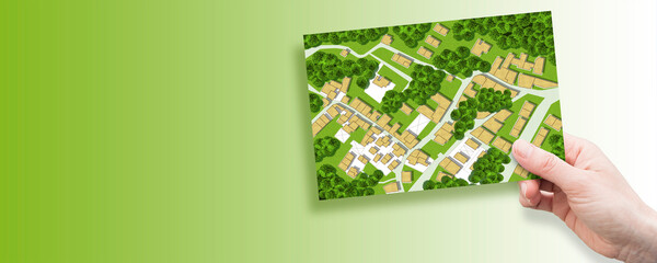 Imaginary city map with residential buildings, roads, gardens green areas and trees - green city concept with a female hand holding a postcard and copyspace