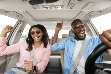 Happy black couple enjoying music driving luxury car