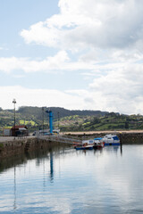 Fototapeta premium Vertical shot of asturian coast. Small harbour at El Puntal with two boats. Calm water, cloudy sky
