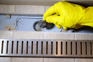 Removing clogged shower drain, gloved hand removes hair